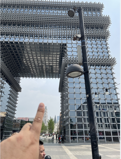 手指指向东北方一座巨大的门洞式网格玻璃建筑，中间镂空形成一个巨大的方形通道