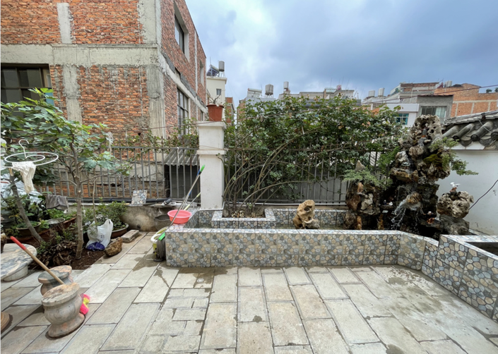 调整后的院落：地面整洁，砌起一圈马赛克瓷砖花池，角落摆放着一组假山石，背后是红砖楼房