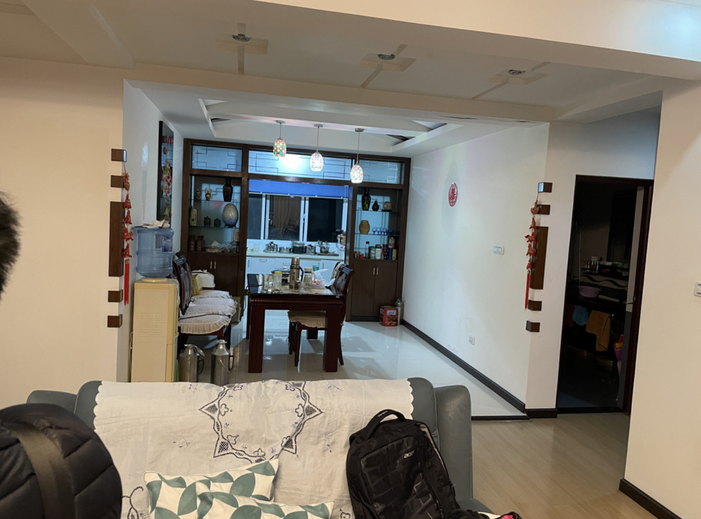 从客厅沙发后方望向餐厅，餐桌后是带玻璃柜和窗户的厨房区域，右侧有一扇通往里间的门
