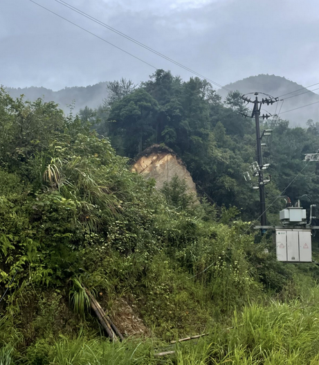 坤方远处的山坡：满山绿树中间露出一大块黄色裸土，像被削掉一块的破损山体，右侧是电线杆和配电箱