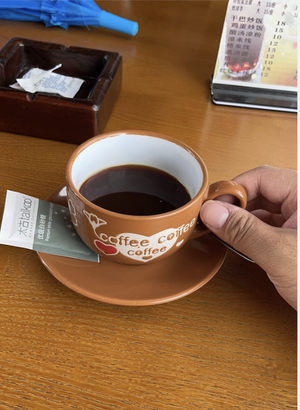 桌上一只印着 coffee 字样的棕色大咖啡杯，杯里满满一杯黑咖啡，旁边是烟灰缸和菜单