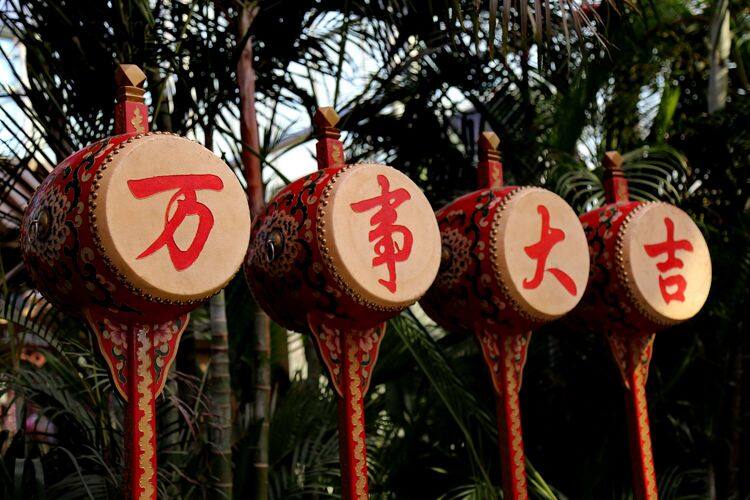 四面并排的红色拨浪鼓式大鼓，鼓面依次写着红字「万」「事」「大」「吉」，背景是棕榈树叶
