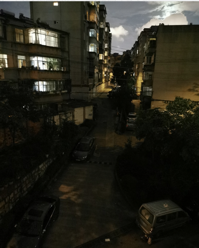夜里从楼上俯拍：一条两侧停着车的小巷笔直延伸，正对着这栋楼