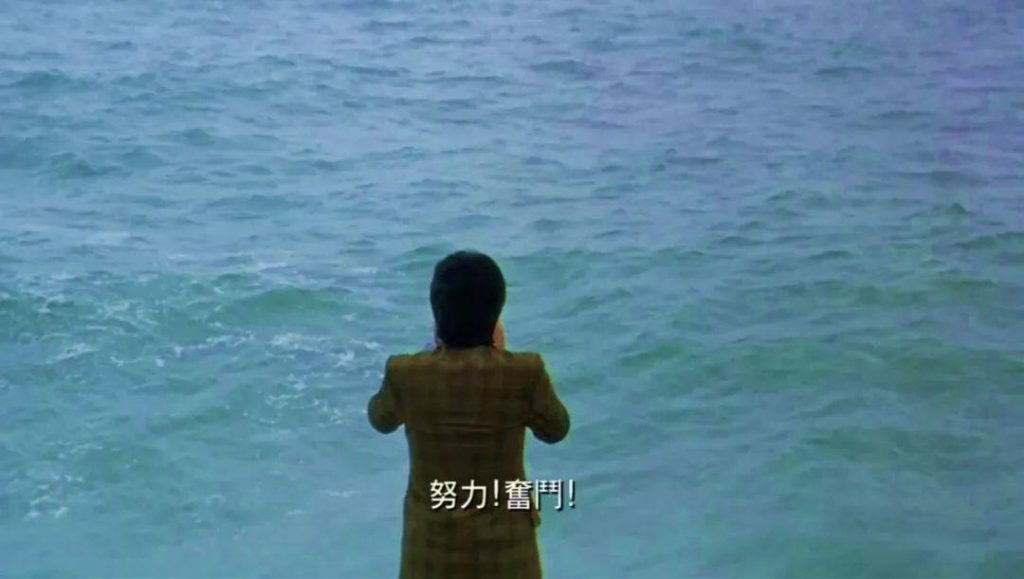 电影截图：一人背对镜头面朝大海，双手拢在嘴边呐喊，字幕为「努力！奋斗！」