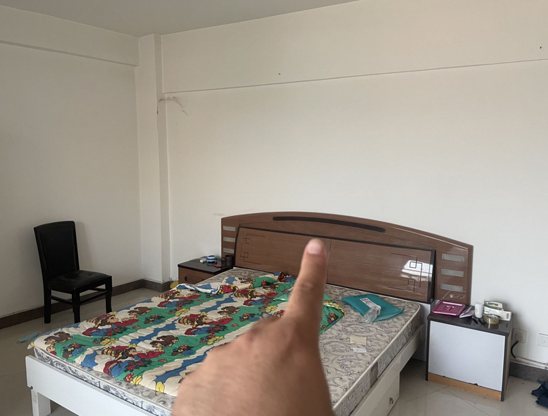 卧室内，手指指向床头后方的墙面：墙体在这一侧转折，是坤位缺角的位置
