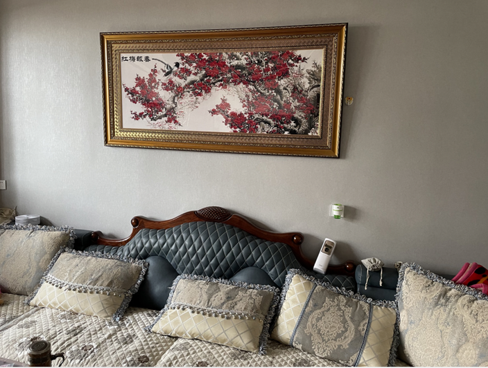 客厅沙发上方挂着一幅金色画框的红梅图，满幅红色梅花，画上题有红梅报春字样
