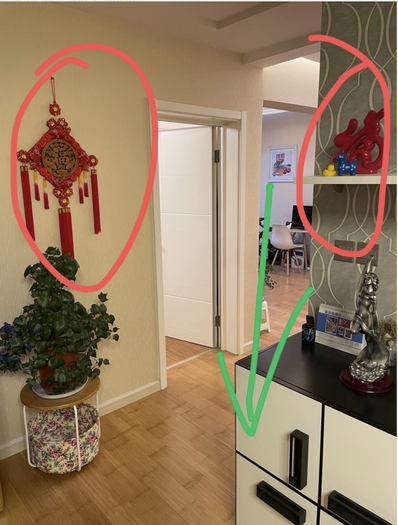 同一张过道照片的标注版：红圈圈出墙上的红色中国结和搁板上的红色摆件，一条绿色箭头指向画面下方